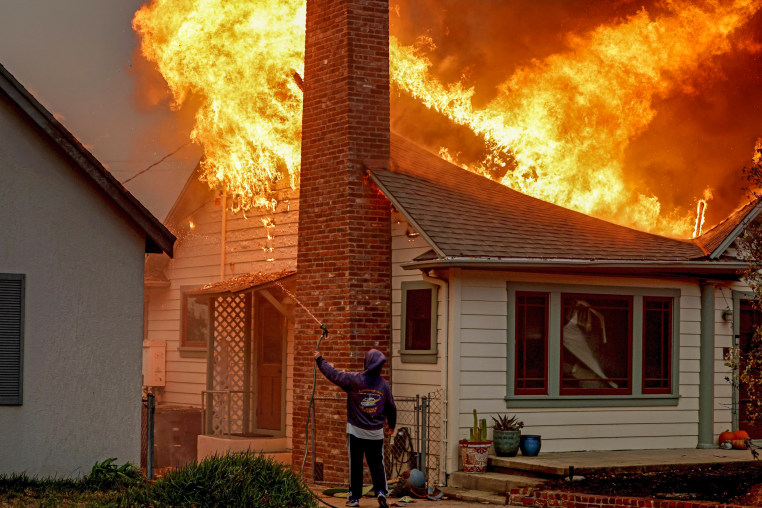 A person turns uses a garden hose in an effort to save a neighboring home.