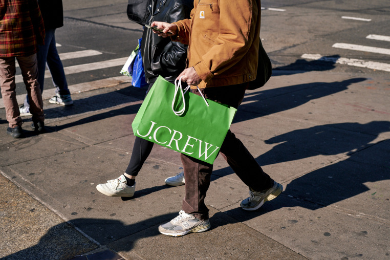 A pedestrian carries a J. Crew shopping bag while walking outside