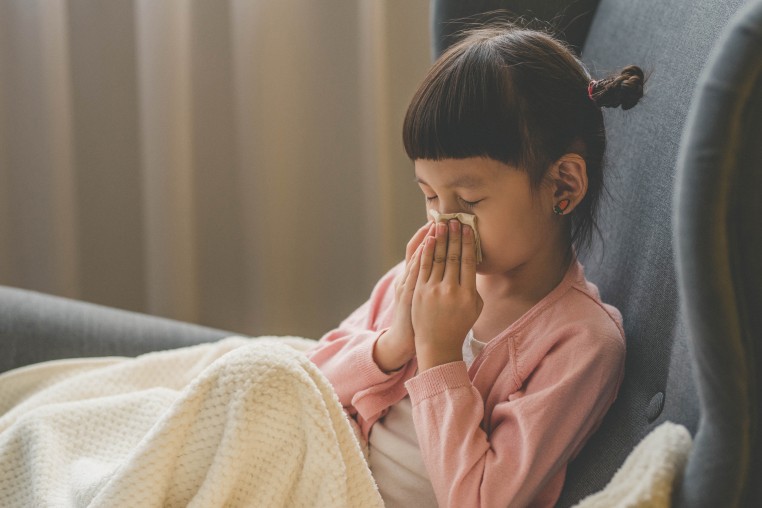 Asian small girl blowing her nose into a napkin