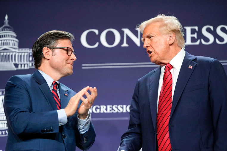 Mike Johnson, left, and Donald Trump speak to each other on stage