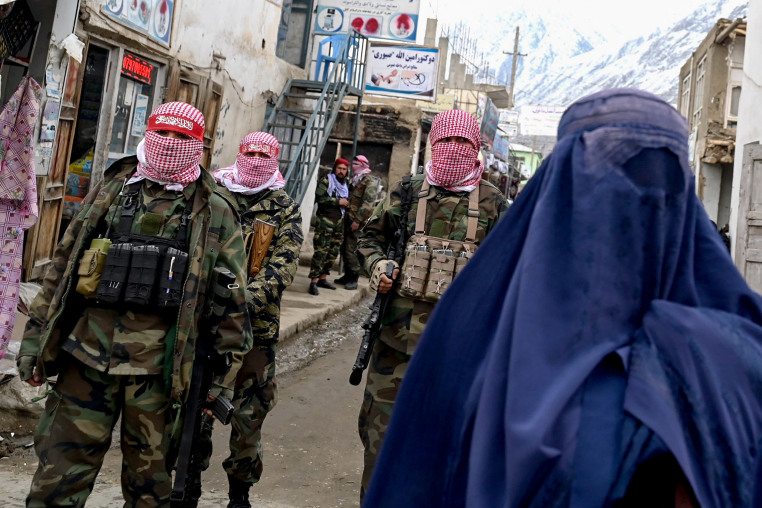 Taliban fighters stand guard as a burqa-clad woman walks along a street