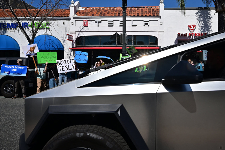 Protesters hold signs that read "Boycott Tesla"