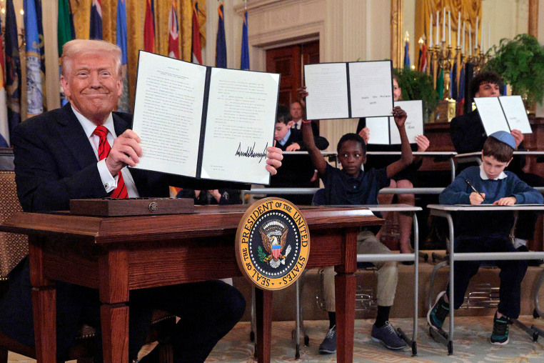 President Donald Trump signs an executive order to reduce the size and scope of the Education Department as school children sign their own versions at the White House on March 20, 2025.