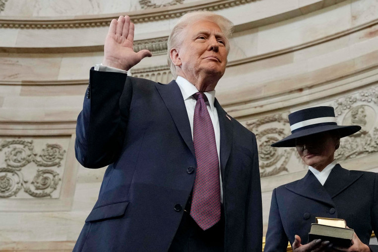 Donald Trump raises his hand as he waits to be sworn in as the 47th president of the United States as Melania Trump holds the Bible in the Rotunda of the Capitol on Jan. 20, 2025.