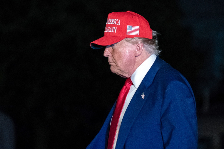 Donald Trump walks outside wearing a red MAGA hat, side profile