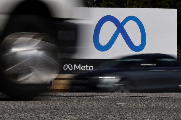 Cars drive past a sign of Meta