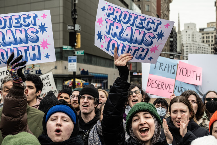 Demonstrators hold signs that read, "Protest Trans Youth."