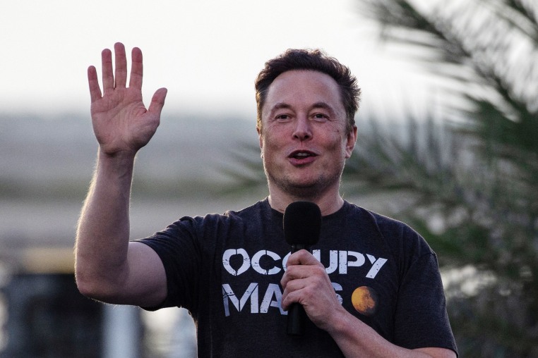 Elon Musk raises his hand while he speaks,