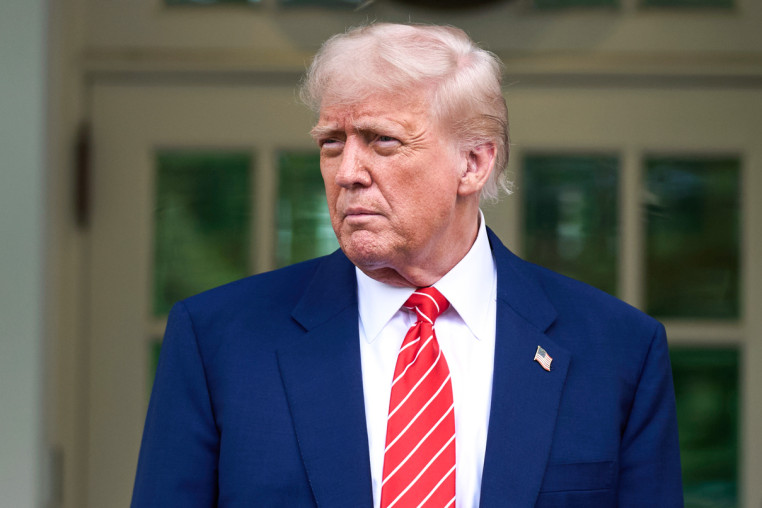 Donald Trump stands outside behind a shrub as a marine in the background salutes him