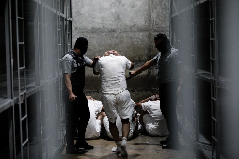 Prisoner led by two security officers inside a cell.