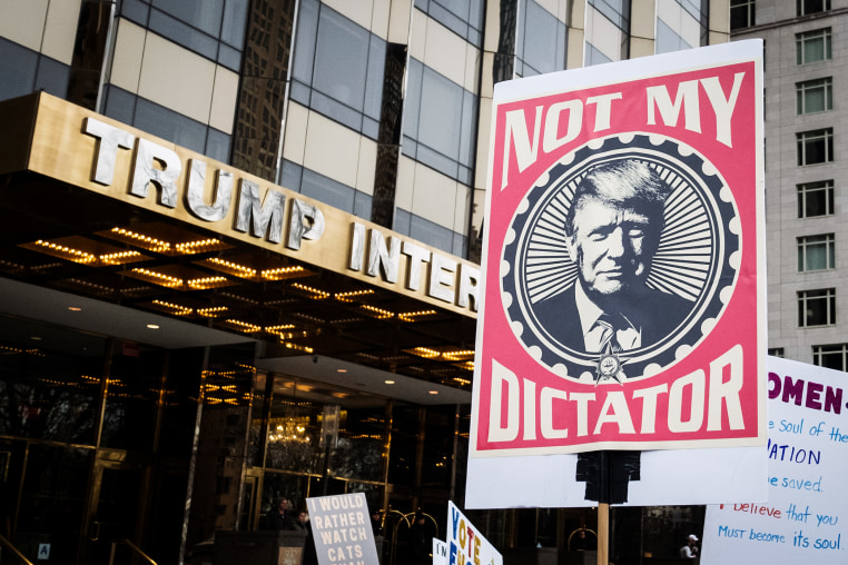  A marcher holds a sign that says, "Not My Dictator" with a picture of Donald Trump in front of Trump International Tower