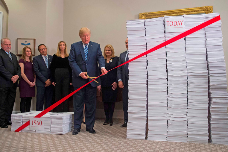 President Donald Trump uses gold scissors to cut red tape between  stacks of papers representing government regulations on Dec. 14, 2017, at the White House.