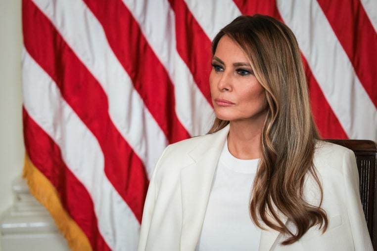 Melania Trump seated in front of an American flag backdrop