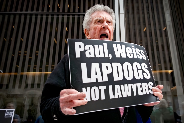 A protester holds a sign that reads, "Paul, Weiss Lapdogs not lawyers"