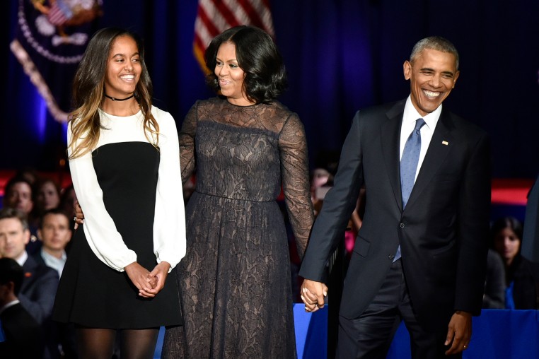From left, Malia Obama, Michelle Obama, and Barack Obama stand on stage
