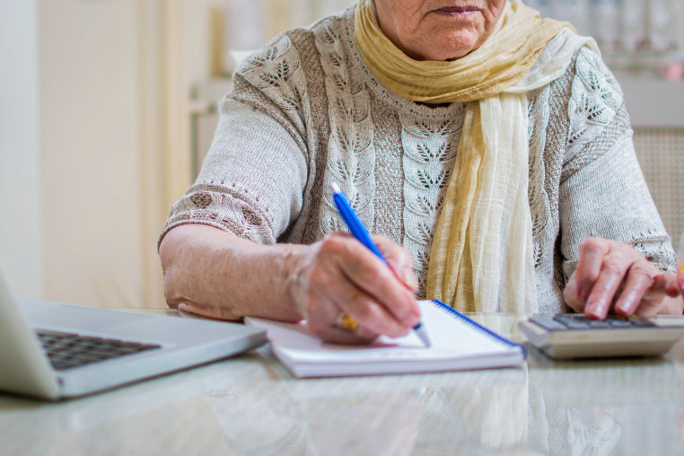Old woman with calculator and notebook calculating gas and electricity bills.