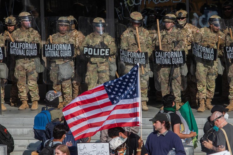 Demonstrators holding signs and flags face California National Guard members standing guard outside the Federal Building 