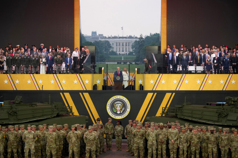 Image: A grandstand with attendees, including Trump and Melania, with soldiers and army tanks below it.