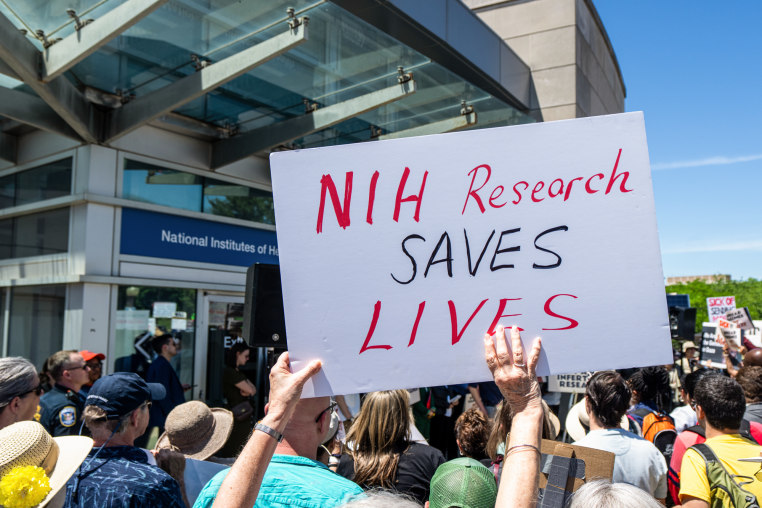 A sign is held in a crowd that says "NIH Research Saves Lives"