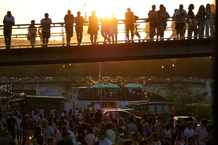 Music enthusiasts gather on bridge and banks of the Seine river during sunset