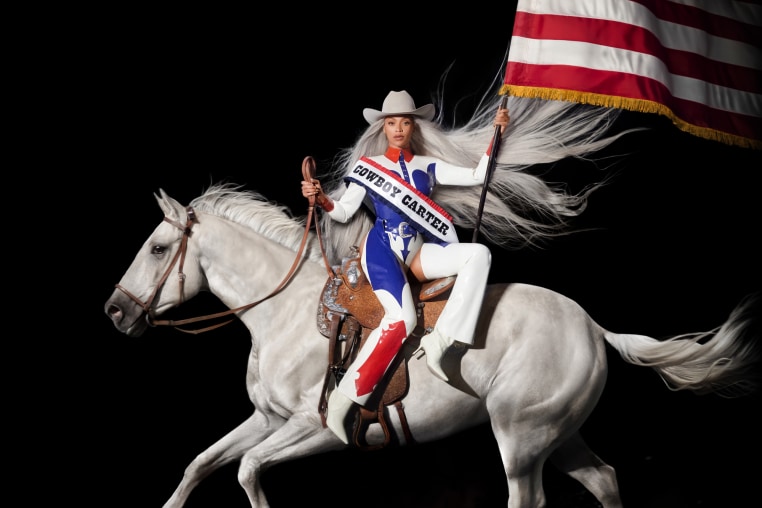 Beyonce sitting on a white horse wearing a sash that says "Cowboy Carter" and waving the American flag