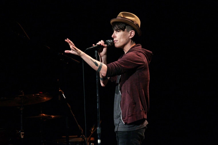 Andrea Gibson speaks into a microphone while standing on stage, one arm outstretched