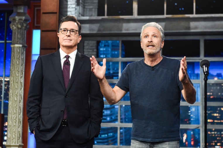 Stephen Colbert, left, and Jon Stewart stand next to each other on stage as Jon speaks