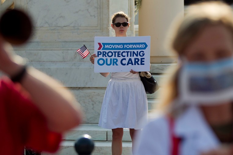 A demonstrator holds a sign that reads, "Moving Forward, Protecting Our Care"