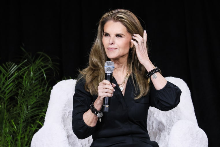Maria Shriver holds a microphone while seated on stage