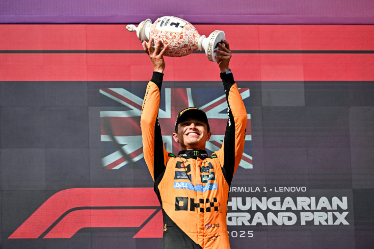 Lando Norris holds a trophy over his head and smiles