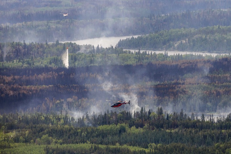 Aerial view of helicopters putting out fires over trees, smoke in the air