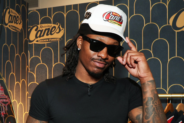Duke Dennis poses in sunglasses and a white Raising Cane's baseball cap