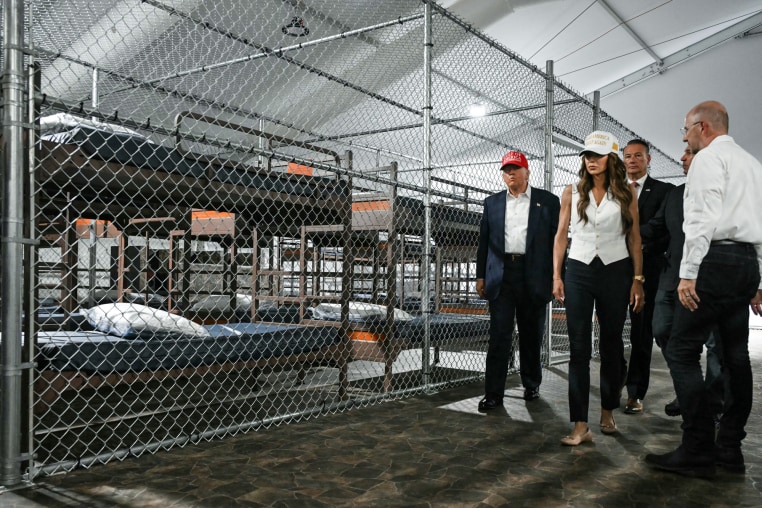 Donald Trump, Kristi Noem, and others walk down a hallway past a prison cell