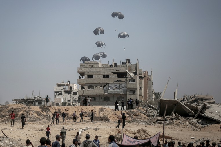Parachutes fall near a partially destroyed building as people approach