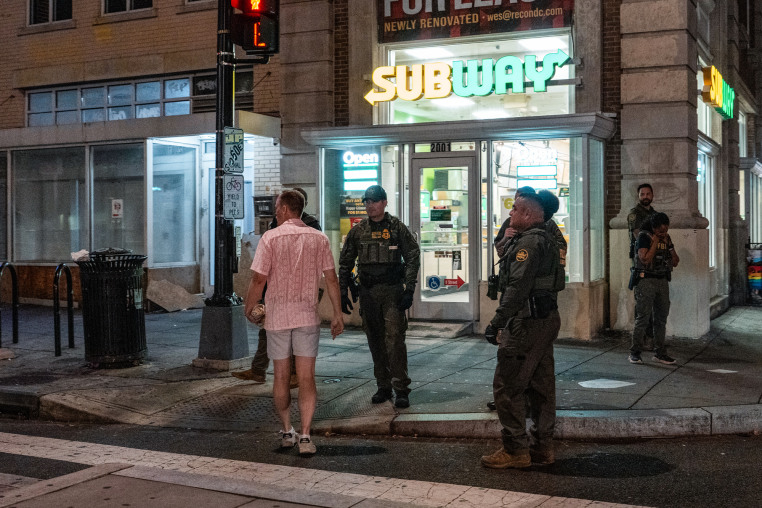 A man walks near officers outside of a Subway location holding a sandwich