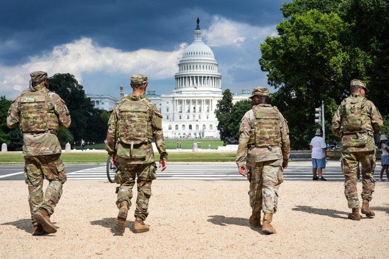 National Guard soldiers walk outside, the U.S. Capitol is seen in the distance