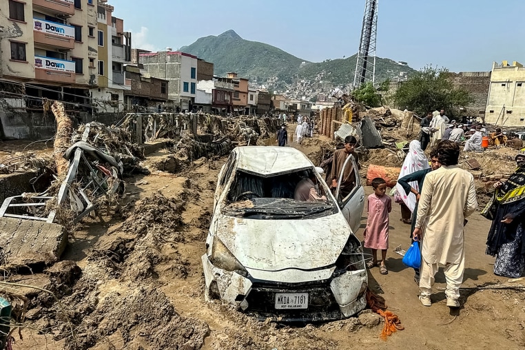 People gather near a damaged vehicle and scattered debris after  a flood