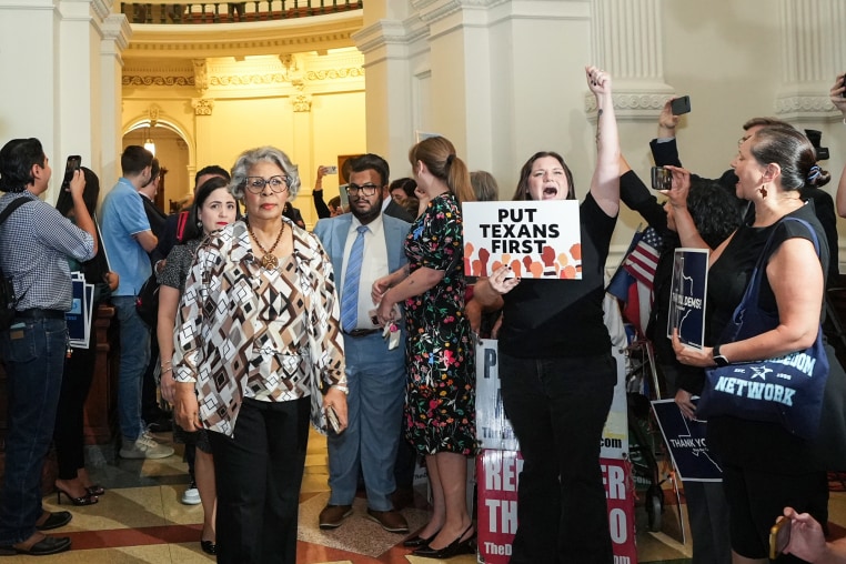 Senfronia Thompson, left, walks past a crowd of people into the House Chamber, a person holds a sign that says "put Texans first"