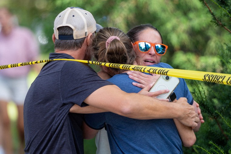 Three people embrace outside underneath caution tape