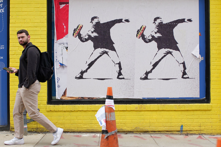 A person walks past Banksy-style posters of a protester throwing a sandwich on Aug. 21, 2025.