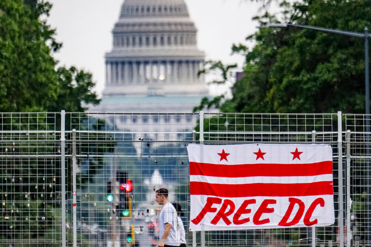 Image: Pedestrians walk past a flag that reads "Free DC" hanging on an overpass near the U.S. Capitol building