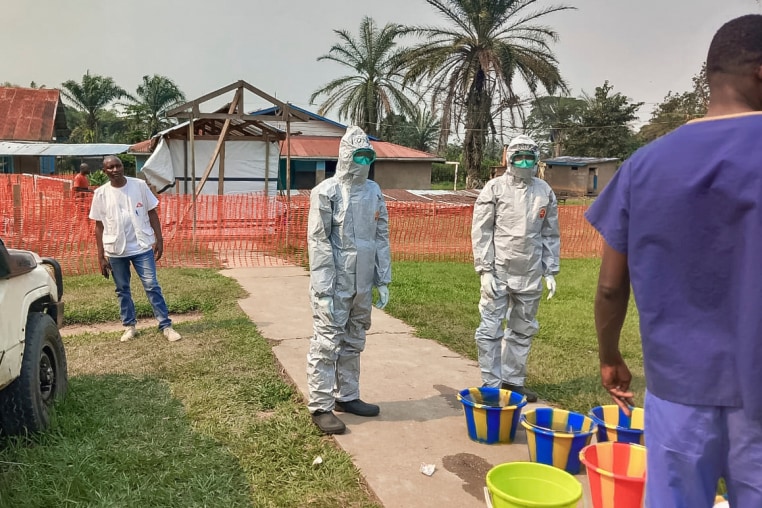 Men in hazmat suits stand outside