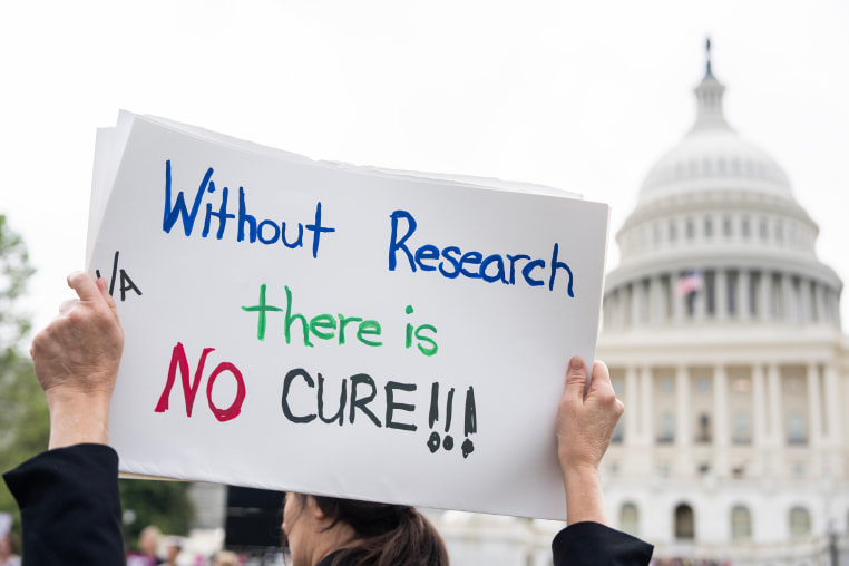A protesters holds a  sign that reads, "Without Research There Is No Cure" outside the Capitol