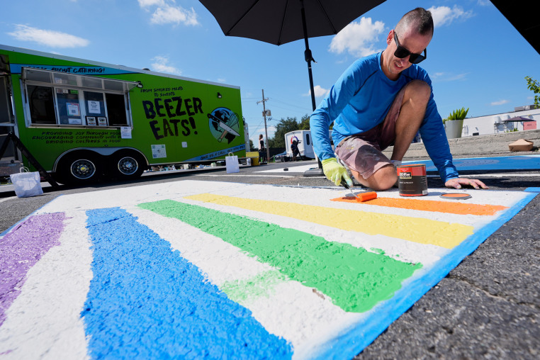 A person paints colored strips in a parking spot outside