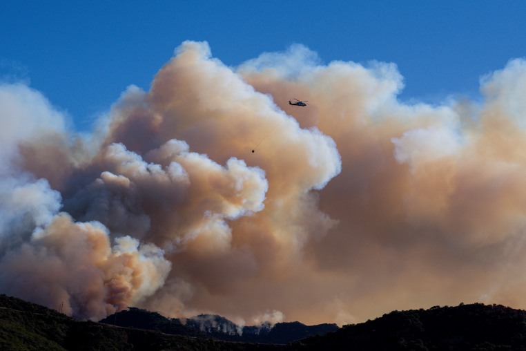 A helicopter flies above clouds of smoke