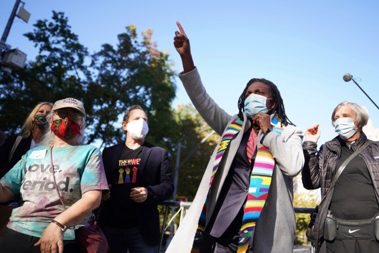 Jacqui Lewis speaks outside while wearing a facemask, point upwards