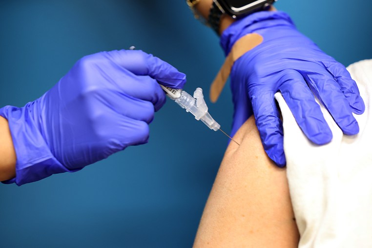 Gloved hands administer a vaccine to a persons shoulder.