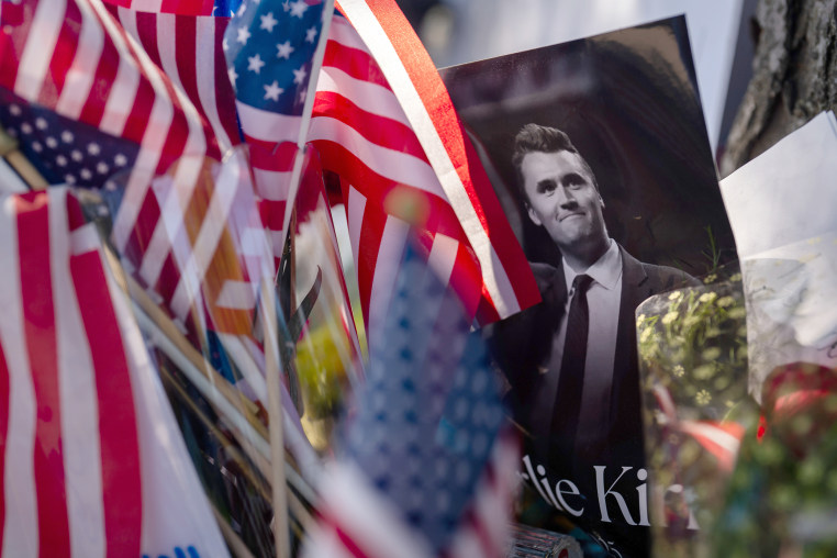 A picture of Charlie Kirk in a memorial surrounded by American flags and flowers