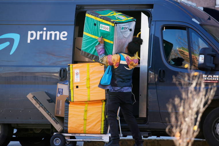 An Amazon Prime delivery person lifts packages while making a stop 