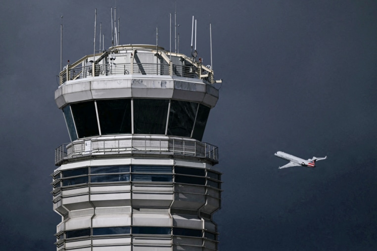 An airplane flies near a control tower on a dark cloudy day